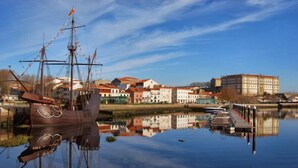 A historic ship docked at a calm harbor with a row of buildings in the background.