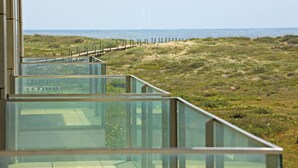 A modern building with a glass balcony overlooking a beach.