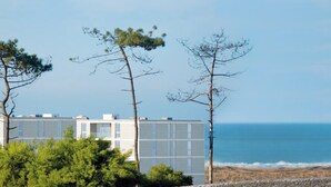 A coastal building with a modern design, surrounded by trees and overlooking the ocean.