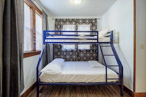 A bunk bed with a headboard, a window with blinds, patterned wallpaper, and a wooden floor. - Eccentric Escape-hop, skip, jump to Plaza District (Oklahoma City)