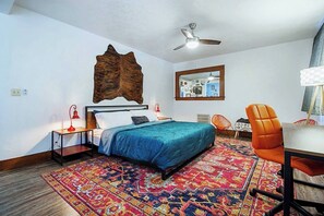 A bedroom with a bed, a desk, an orange chair, a patterned rug, a ceiling fan, and a wall-mounted mirror. - Eccentric Escape-hop, skip, jump to Plaza District (Oklahoma City)