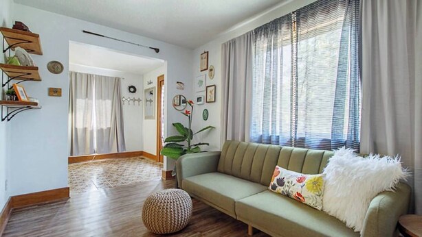 A living room with a sofa, a patterned rug, a potted plant, and a wooden floor. - Eccentric Escape-hop, skip, jump to Plaza District (Oklahoma City)