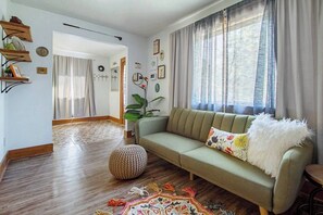 A living room with a sofa, a patterned rug, a potted plant, and a wooden floor. - Eccentric Escape-hop, skip, jump to Plaza District (Oklahoma City)