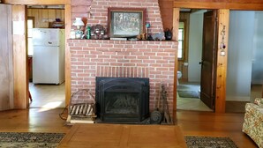 A cozy living room with a brick fireplace, wooden beams, and a patterned rug.