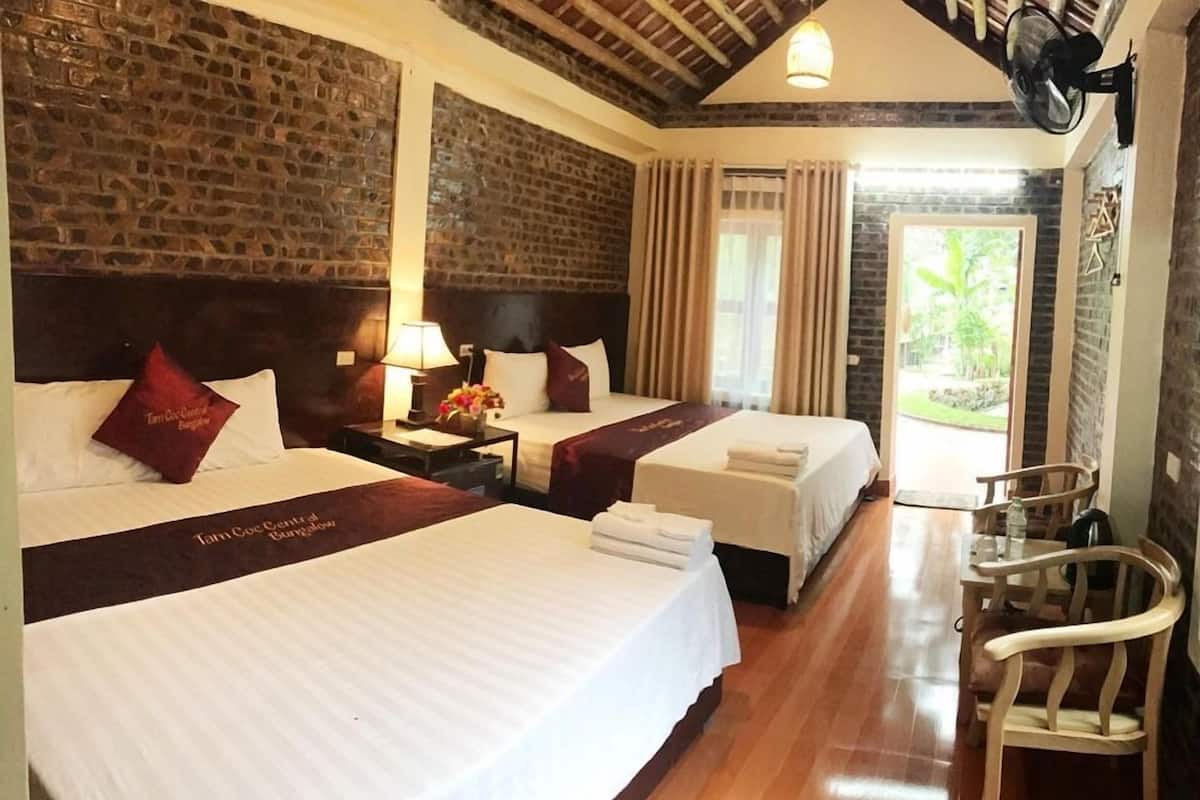 A hotel room with two beds, a wooden floor, a brick wall, and a view of the outdoors.