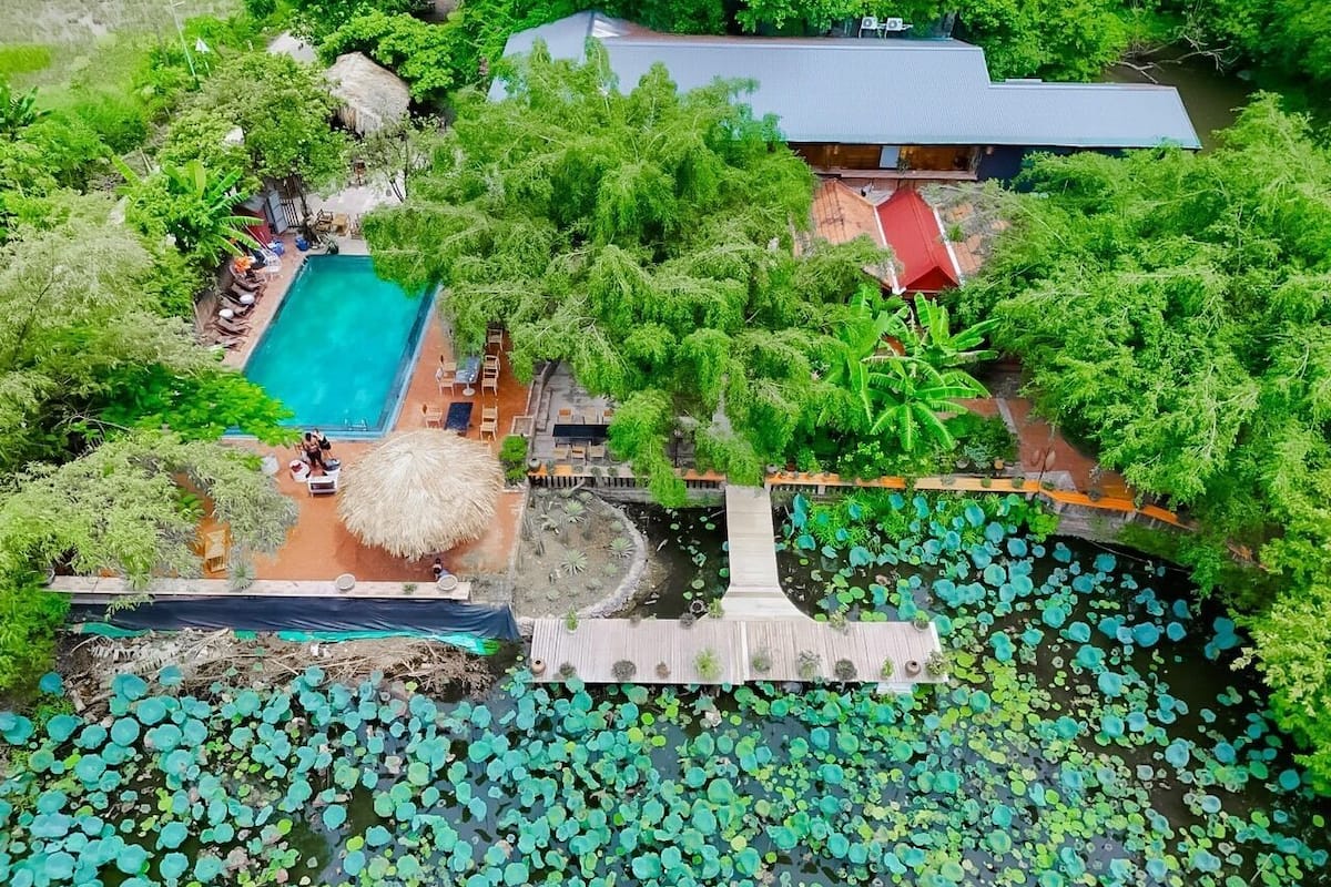 An aerial view of a resort with a swimming pool, a wooden deck, and a pond with lily pads.