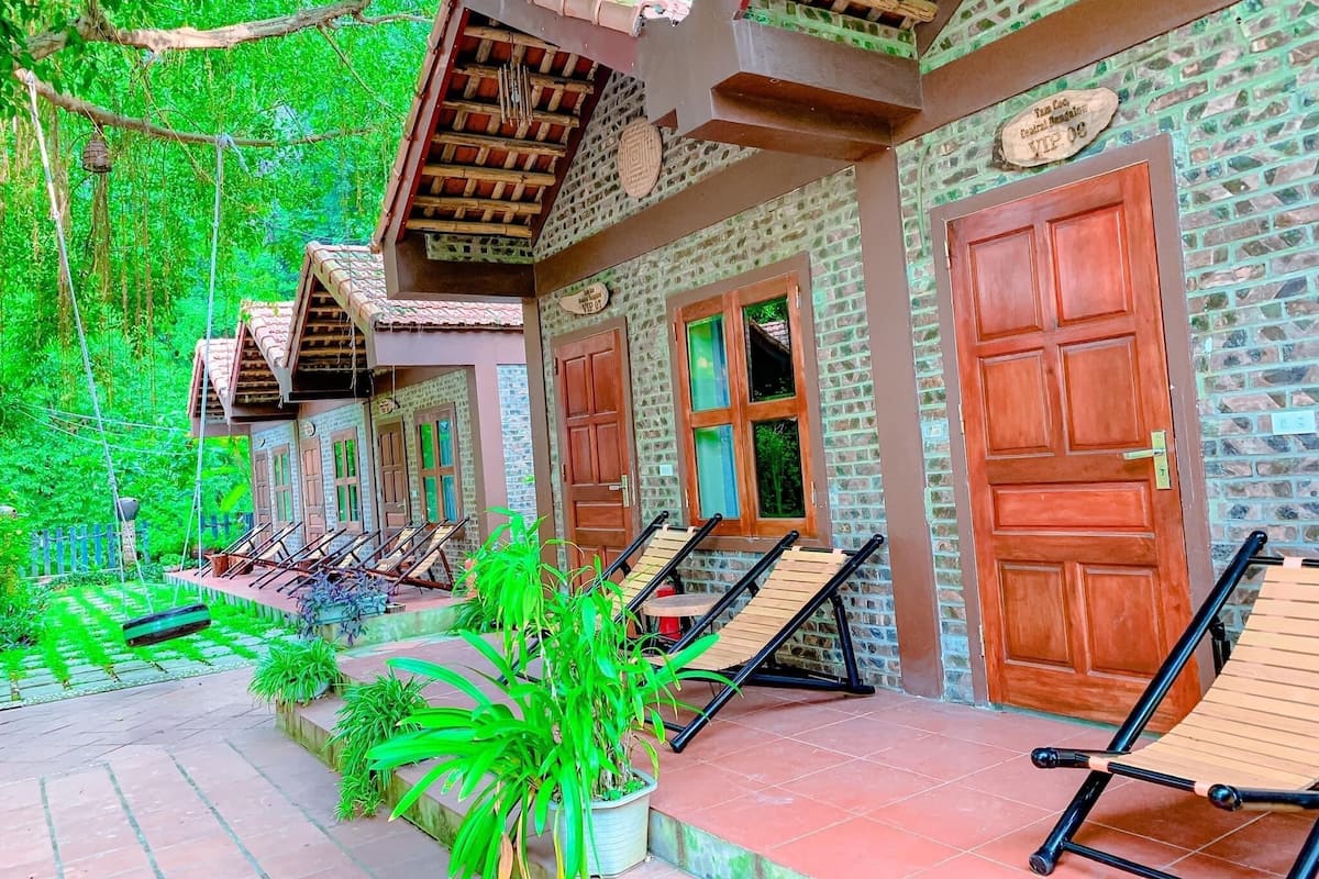 A courtyard with wooden benches and potted plants, surrounded by buildings with brick walls and wooden doors.