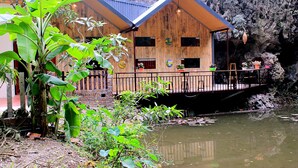 Une maison en bois dotée d’un balcon donnant sur une rivière, entourée d’une végétation luxuriante.