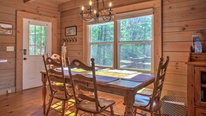A wooden interior with a dining table, chairs, a chandelier, and large windows. - Pet-Friendly Log Cabin with Hot Tub & Biltmore Pass | 35 Min to Asheville (Waynesville)