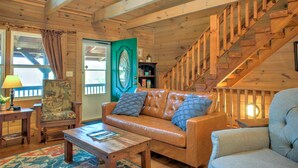 A wooden interior with a leather sofa, a wooden coffee table, a patterned armchair, and a staircase. - Pet-Friendly Log Cabin with Hot Tub & Biltmore Pass | 35 Min to Asheville (Waynesville)