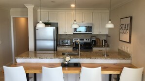 Una cocina moderna con armarios blancos, encimeras de granito, electrodomésticos de acero inoxidable y una mesa de comedor de madera con sillas blancas.