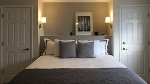 Un dormitorio ordenado con una cama, un ventilador de techo, dos lámparas de pared y un cuadro en la pared.