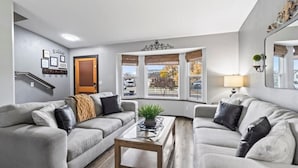 A modern living room with two grey sofas, a wooden coffee table, and a large window with a view of the outside. - Hot Tub Gameroom Great Location Sparkling Clean (West Valley City)