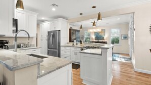 A modern kitchen with white cabinetry, stainless steel appliances, and a central island. - 5-bedroom vacation home in the Village with just a short walk to Captiva Beach! (Captiva)