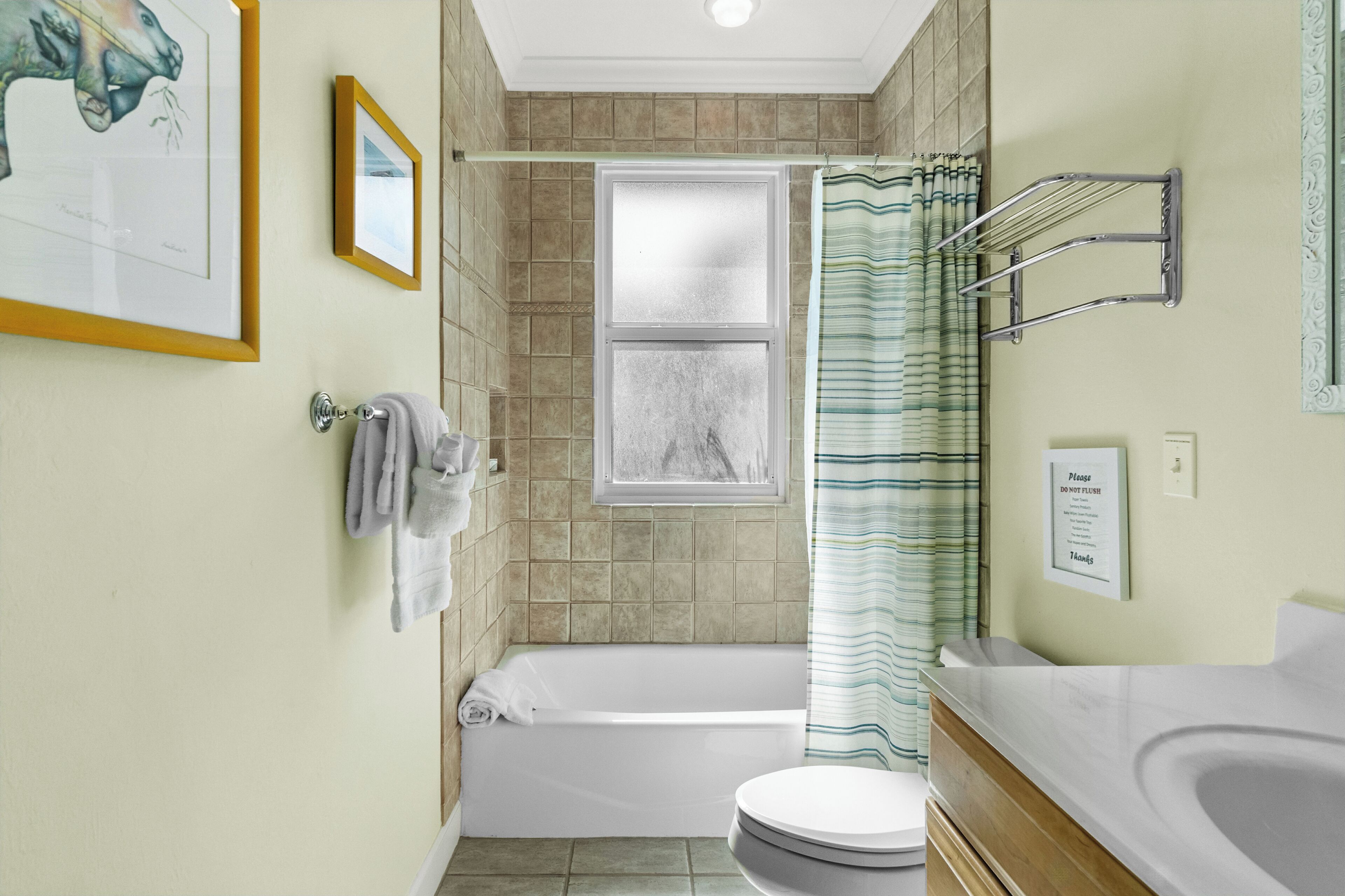 Une salle de bain équipée d’une baignoire, de toilettes, d’un lavabo, d’un porte-serviettes, d’un tableau encadré et d’un panneau indiquant : « Veuillez ne pas tirer la chasse d’eau ».