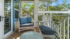 A balcony with wicker furniture, a glass door, and a view of palm trees. - 5-bedroom vacation home in the Village with just a short walk to Captiva Beach! (Captiva)