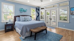 A bedroom with a bed, a bench, a nightstand, a ceiling fan, and large windows. - 5-bedroom vacation home in the Village with just a short walk to Captiva Beach! (Captiva)