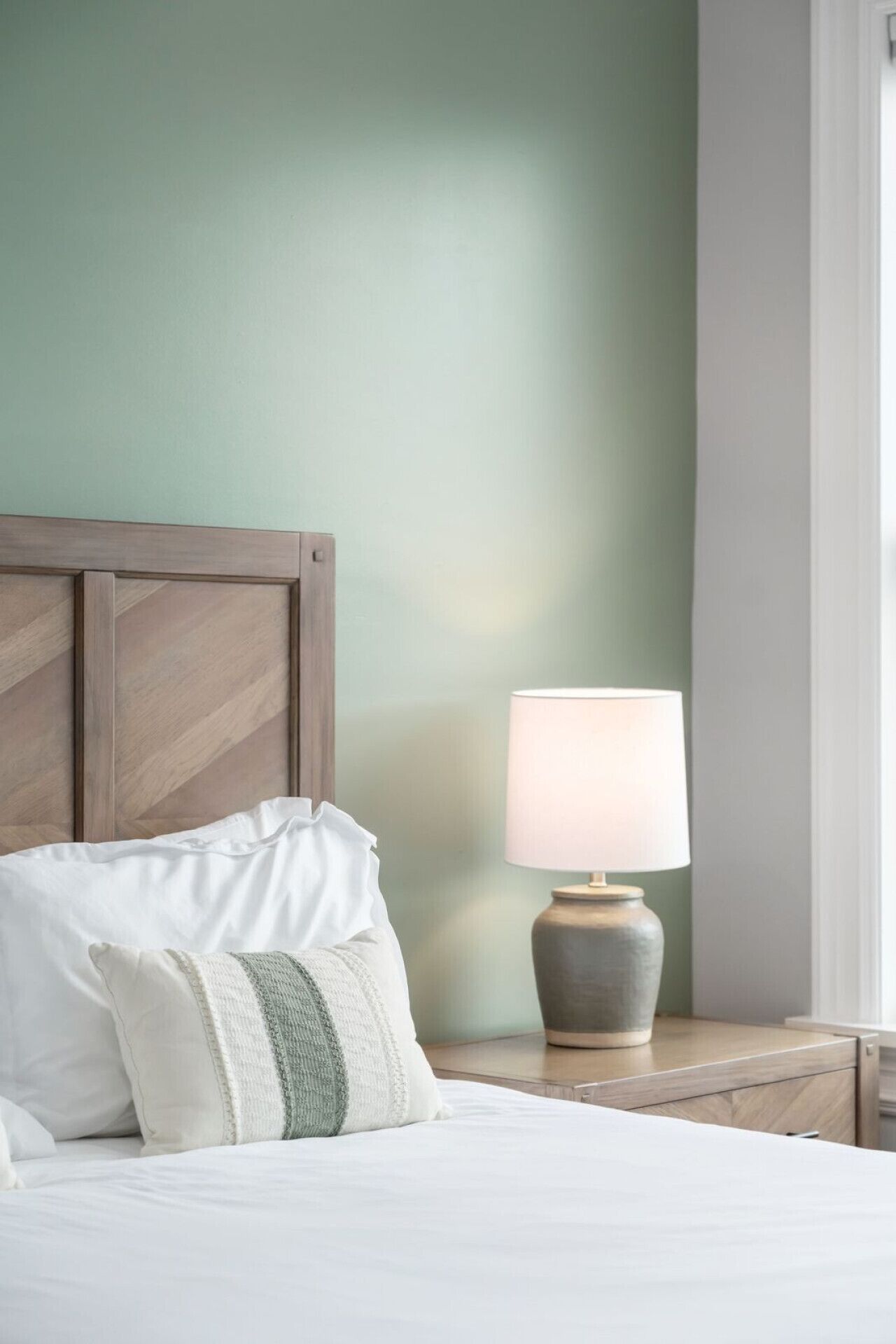A neatly made bed with pillows, a wooden headboard, and a bedside table with a lamp.
