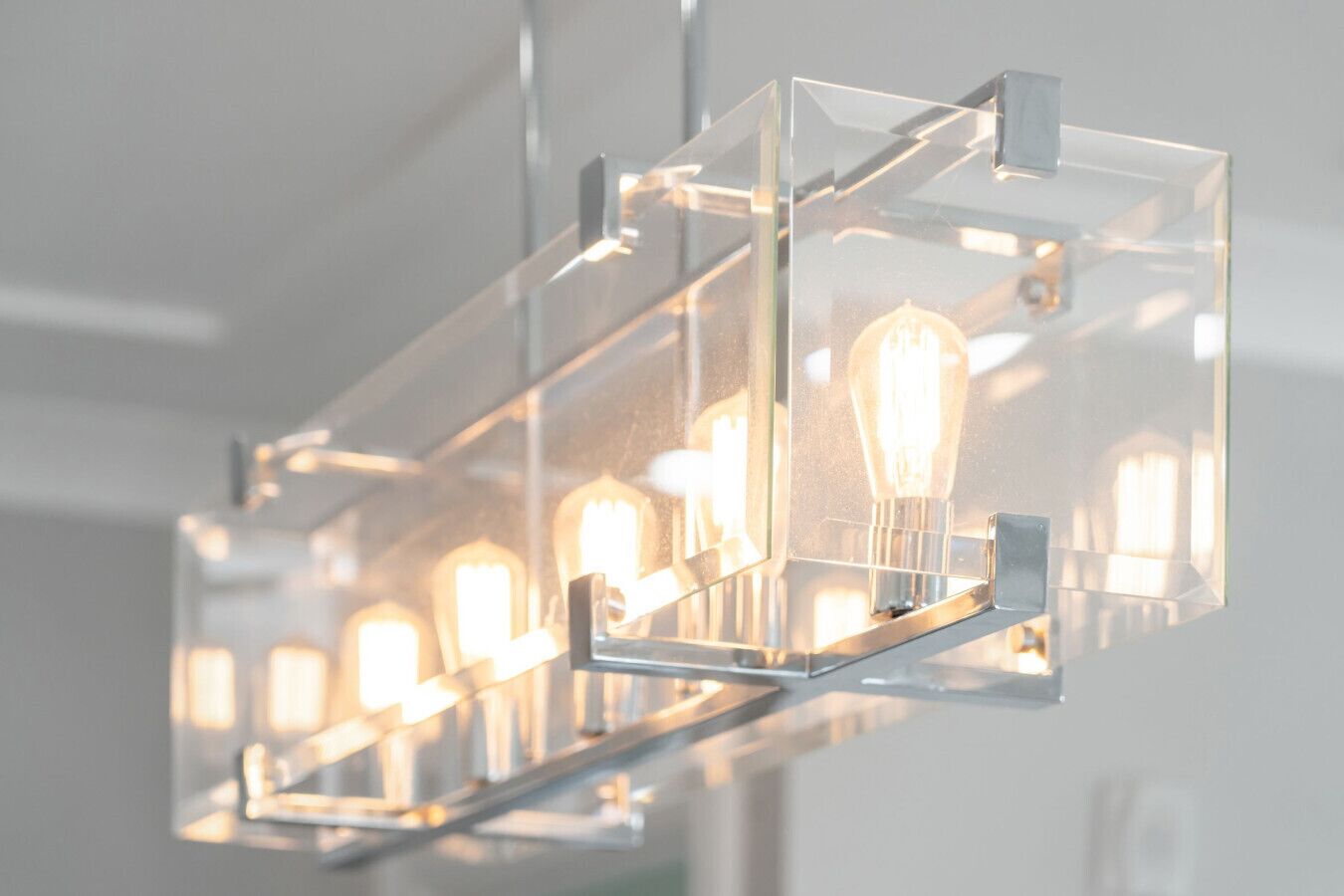 Un lustre moderne doté de plusieurs ampoules, le tout intégré dans une structure géométrique transparente.