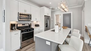 Una cocina moderna con armarios blancos, electrodomésticos de acero inoxidable y una isla central con taburetes de bar.