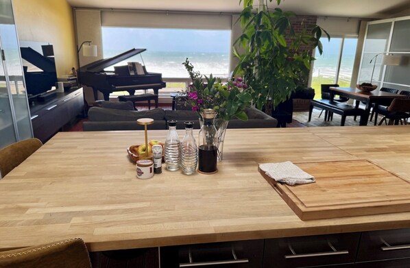 A dining area with a wooden table, a piano, and a view of the ocean.