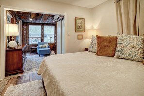 Ein Schlafzimmer mit einem großen Bett, einem Schreibtisch mit Lampe, einem Sessel und einem Fenster mit Jalousien.