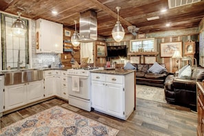 A spacious kitchen with white cabinetry, a central island, and a dining area with a brown leather couch. - River Bungalow on the Colorado River 2 Miles From Historic Bastrop, Texas (Bastrop)