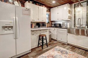 A kitchen with white cabinets, a refrigerator, a water dispenser, a wooden stool, and a patterned rug. - River Bungalow on the Colorado River 2 Miles From Historic Bastrop, Texas (Bastrop)