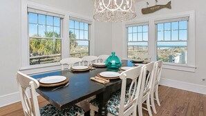 A dining room with a dark wooden table, white chairs with patterned cushions, and a view of the beach through large windows. - Relaxed Cancellation Policy! Oceanfront home with pool,hot tub, fire pit, bikes. (St Augustine)