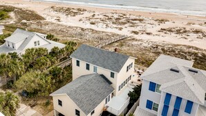 A coastal residential area with houses near a beach, featuring a wooden deck and a view of the ocean. - Relaxed Cancellation Policy! Oceanfront home with pool,hot tub, fire pit, bikes. (St Augustine)