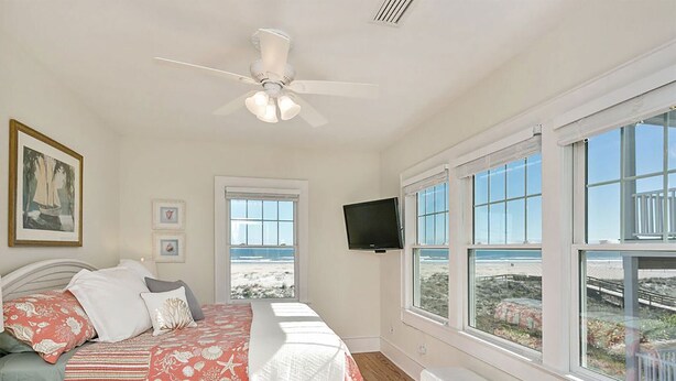 A bedroom with a bed, a ceiling fan, a TV, and large windows with a view of the beach. - Relaxed Cancellation Policy! Oceanfront home with pool,hot tub, fire pit, bikes. (St Augustine)