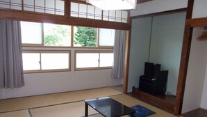 Una habitación con tatamis, una mesa negra, dos esteras azules, un mueble para televisión y una puerta corredera.