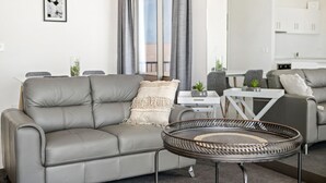 Uma sala de estar moderna com um sofá cinzento, uma mesa de centro redonda de vime e uma mesa lateral branca com uma planta.