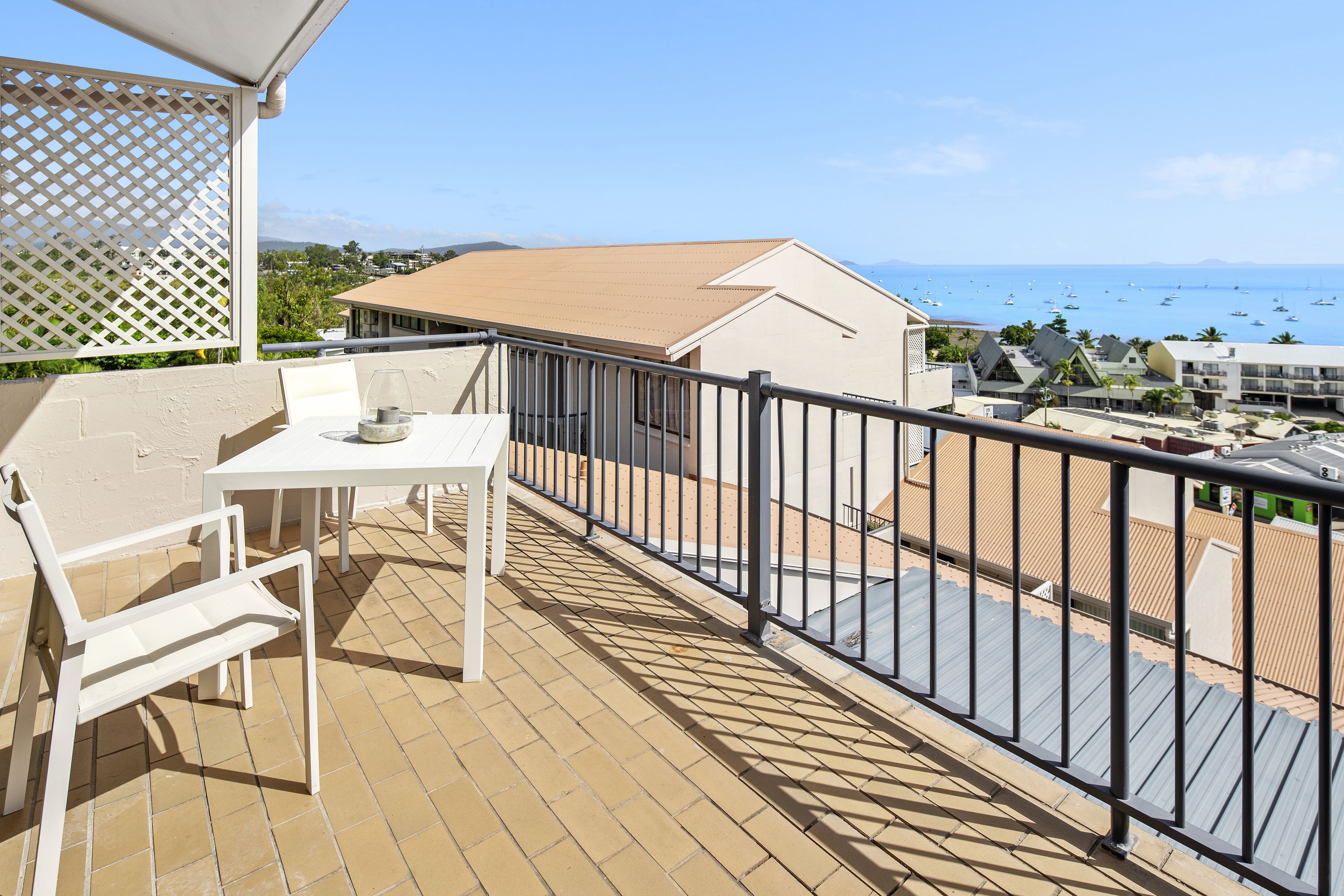 A balcony with a table and chairs, a view of the sea, and buildings in the background.