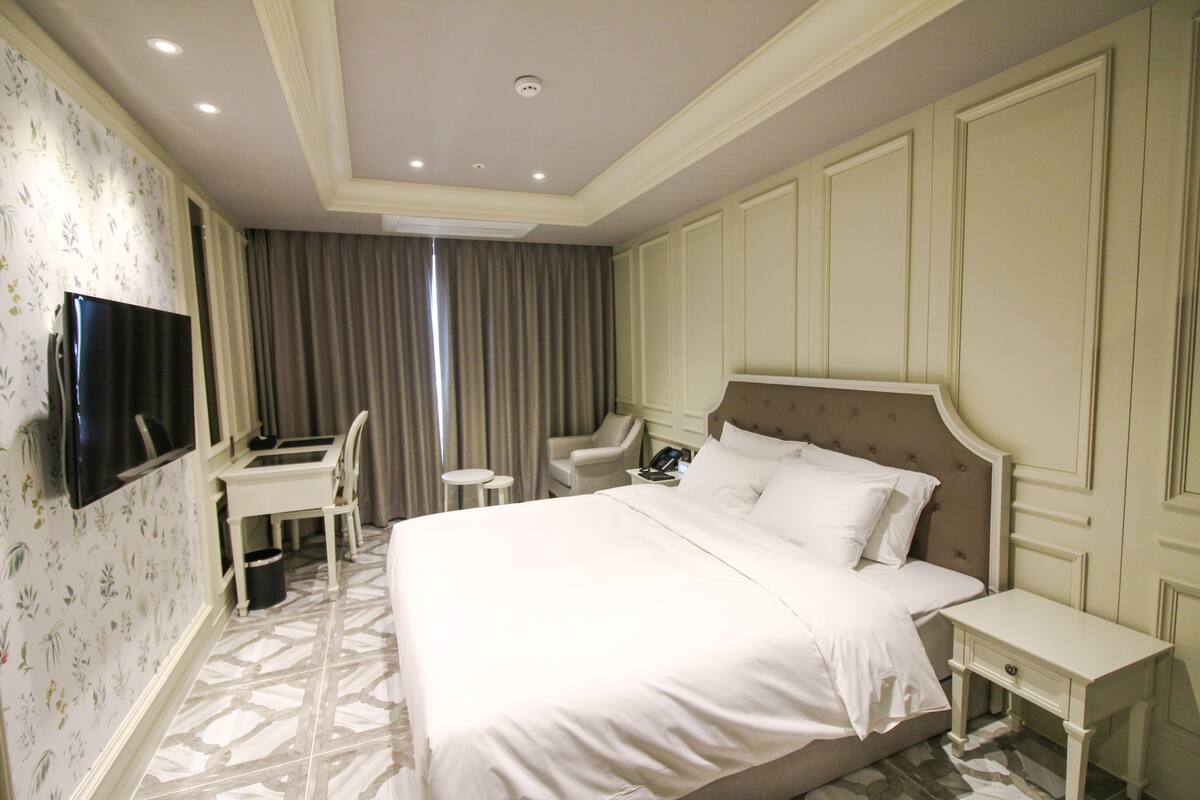 A hotel room with a large bed, a desk with a chair, a television, and a telephone.