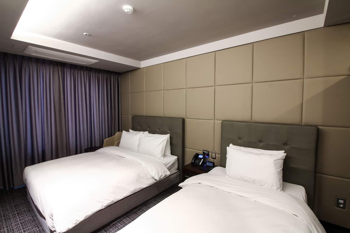 A hotel room with two beds, a bedside table with a phone, and a large window with curtains.