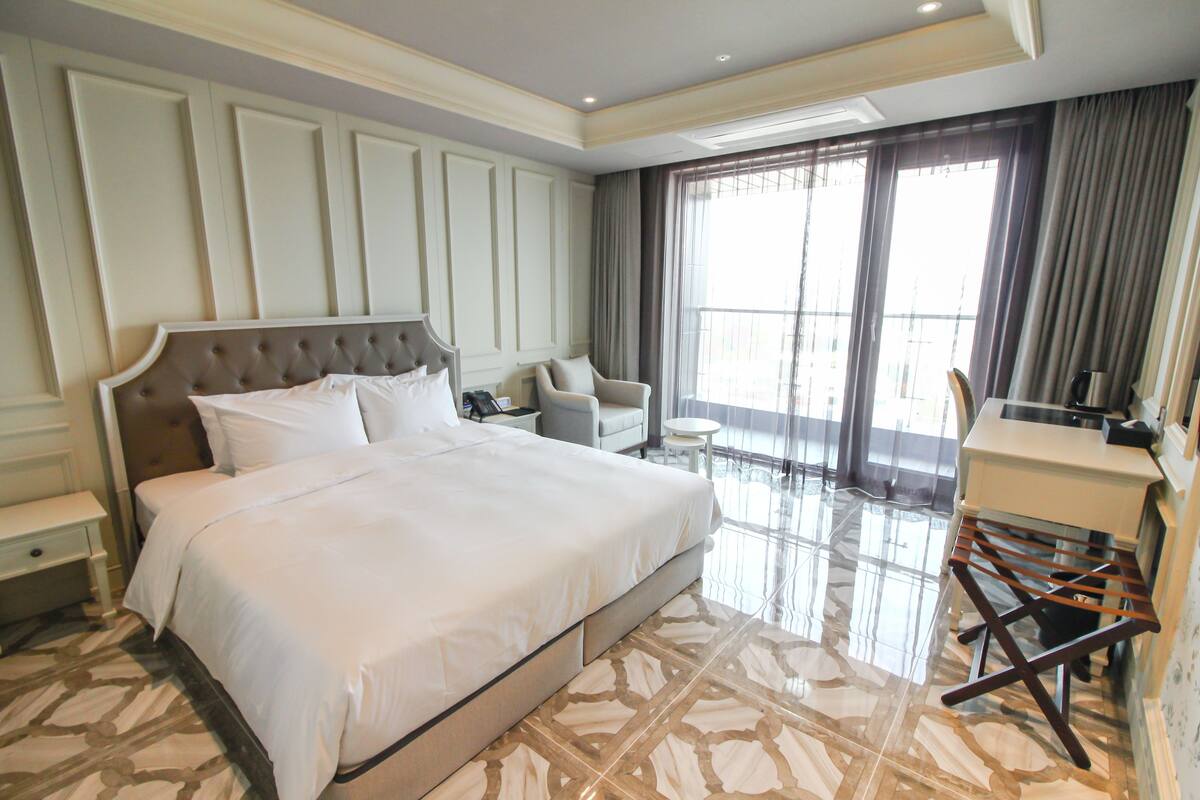 A spacious bedroom with a large bed, a seating area, and a view of the outdoors.