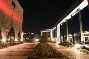 Un edificio moderno con un sendero de ladrillos que conduce a un área de descanso, rodeado de árboles e iluminado con luz artificial.