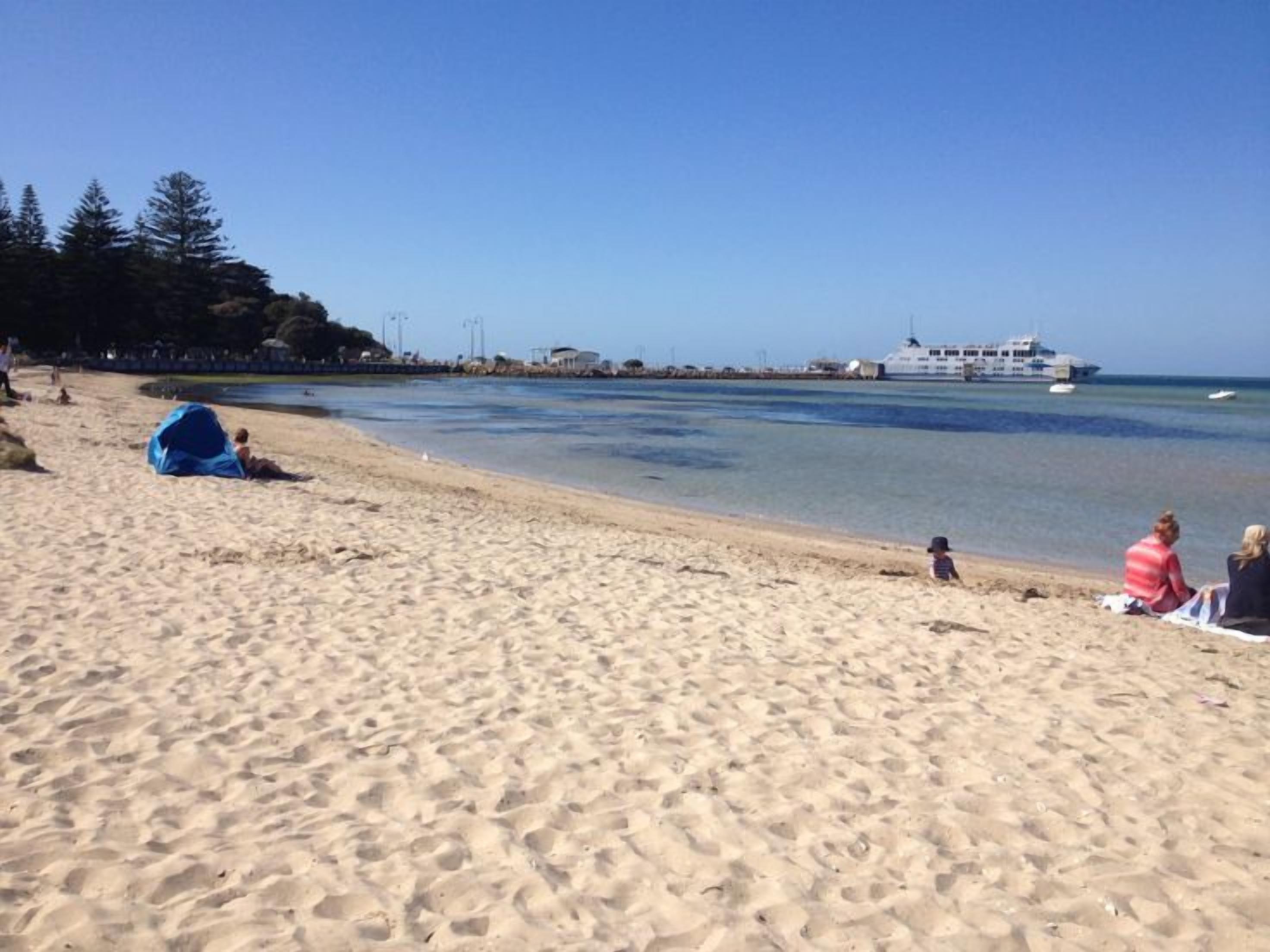 A beach with a sandy shore, a few people, and a large ship in the distance.