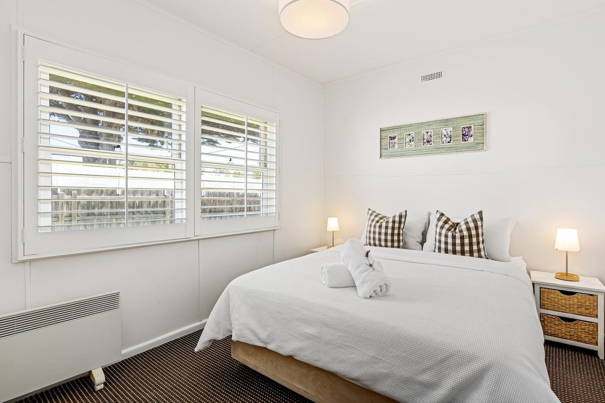 A hotel room with a large bed, two bedside tables, a wall-mounted picture, and a window with blinds.