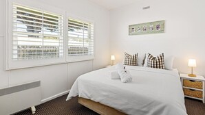 A hotel room with a large bed, two bedside tables with lamps, a radiator, and a window with blinds.