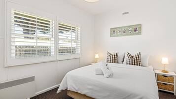 A hotel room with a large bed, two bedside tables, a wall-mounted picture, and a window with blinds.