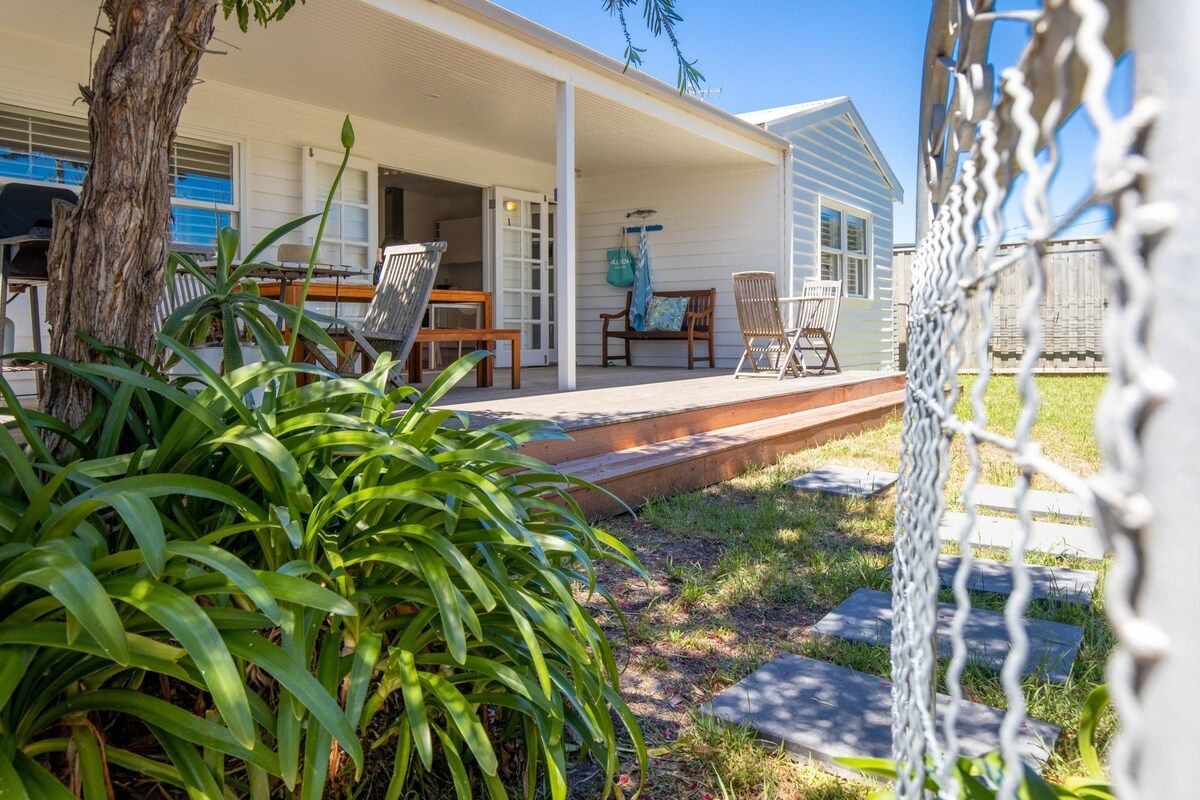 A covered outdoor area with a table and chairs, a bench, and a pathway leading to a house.