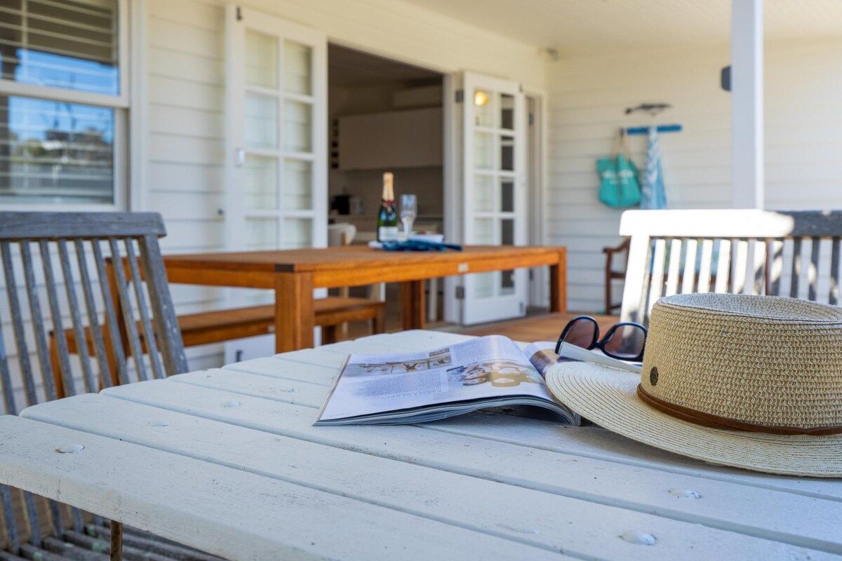 A wooden table with a magazine and a straw hat on it, a wooden bench, and a wooden chair.