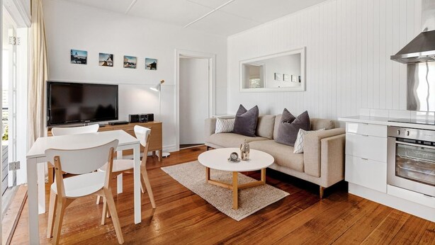 A modern living room with a flat-screen TV, a sofa, a dining table with chairs, and a kitchen area with a stove.
