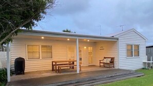 A single-story house with a porch, a bench, and a small table.