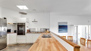 Une cuisine moderne avec des meubles blancs, un îlot central en bois et une grande table à manger.