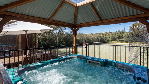 Un espace avec un bain à remous, une terrasse en bois, un coin salon abrité et une vue sur le paysage environnant.
