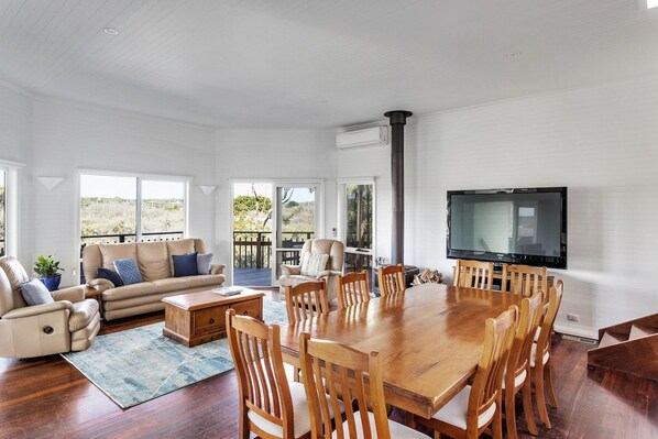 A spacious living room with a large wooden dining table, comfortable seating, and a television.