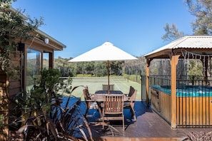 A wooden deck with a table and chairs, a tennis court, and a hot tub area. - The Heyfield Hideaway Rye (RYE)